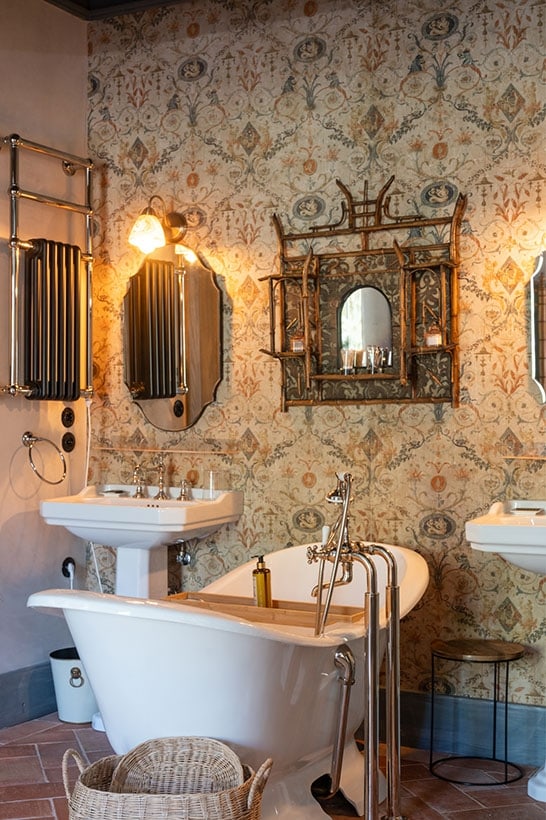 A claw-foot bath beneath hand-painted wallpaper